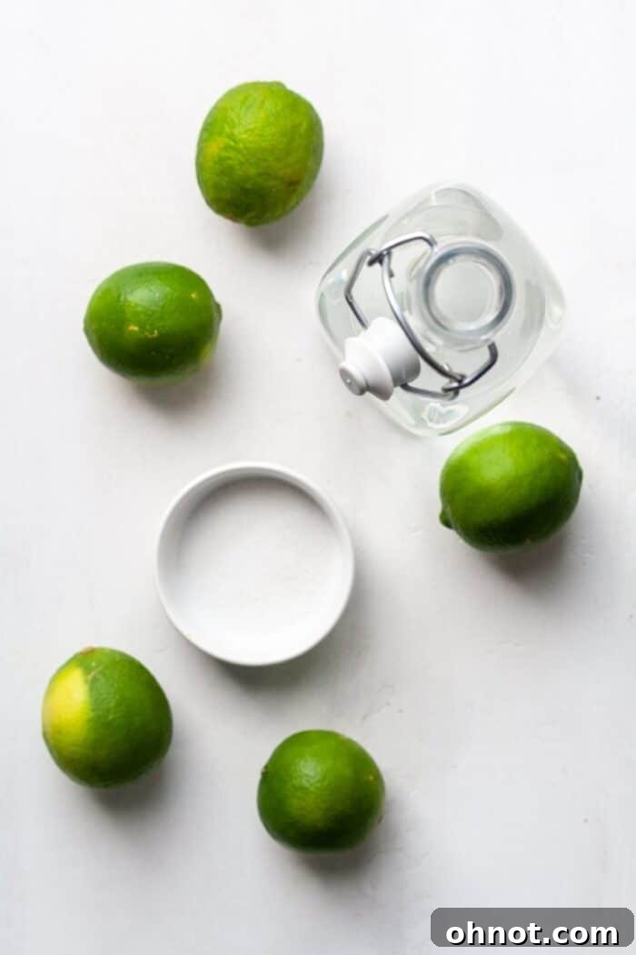 Fresh limes, a glass of water, and a spoon with granulated sugar, illustrating the core ingredients for limeade.