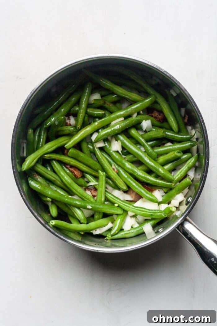 Green beans and bacon cooking in a pot, with onions and garlic