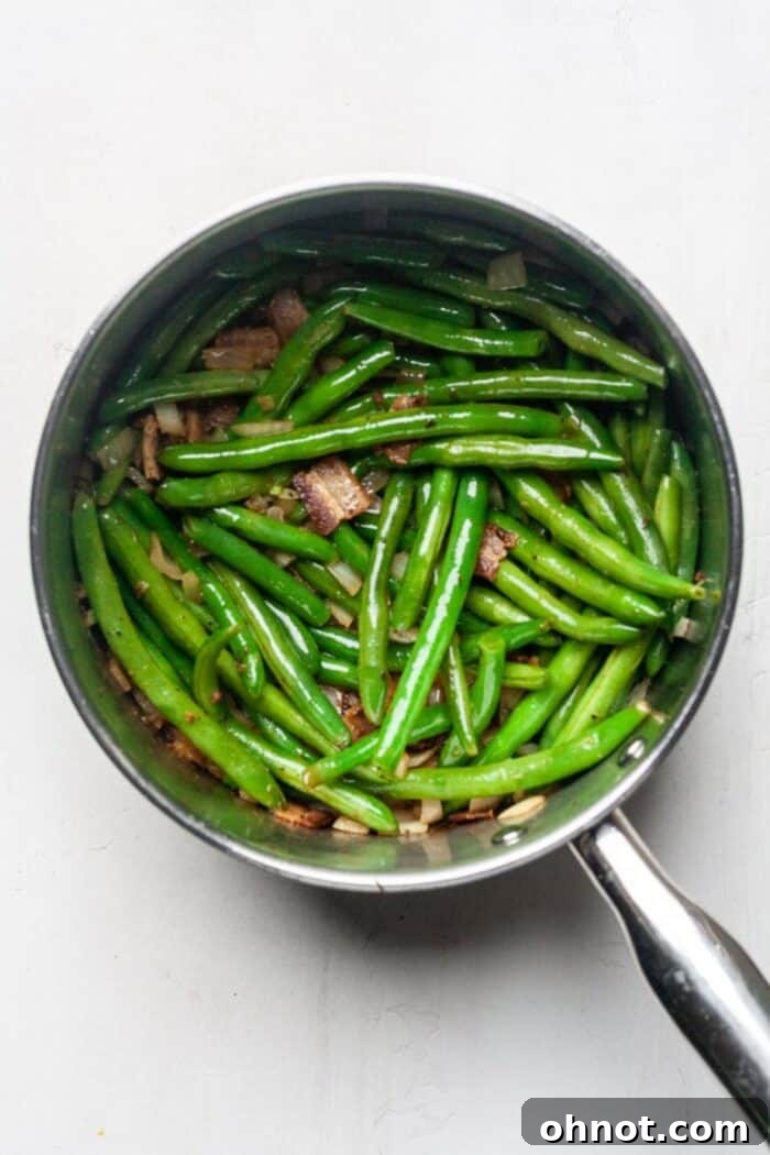 Cooked green beans in a pot with softened onions, garlic, and bacon