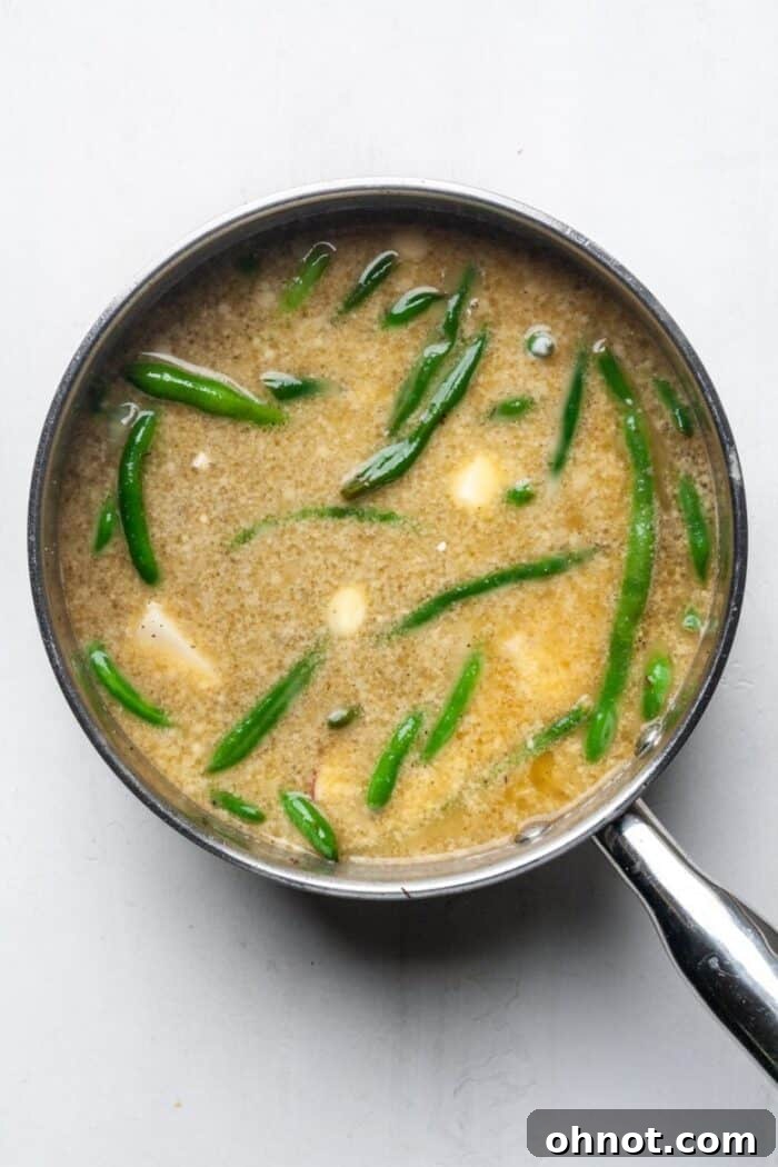Creamy green beans and potatoes mixture boiling in a pot, with broth and butter