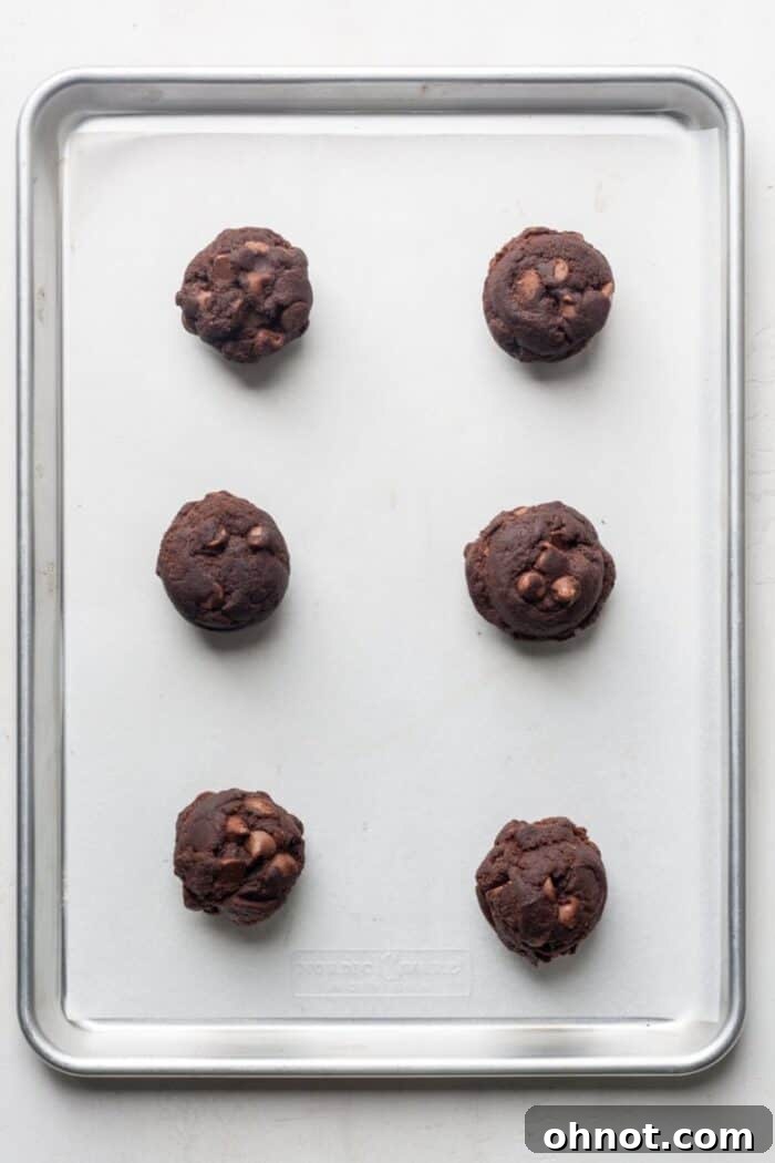 Large balls of chocolate cookie dough on a parchment-lined baking sheet