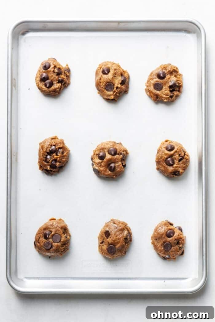 Raw sunflower seed butter cookie dough balls neatly arranged on a parchment-lined baking pan.