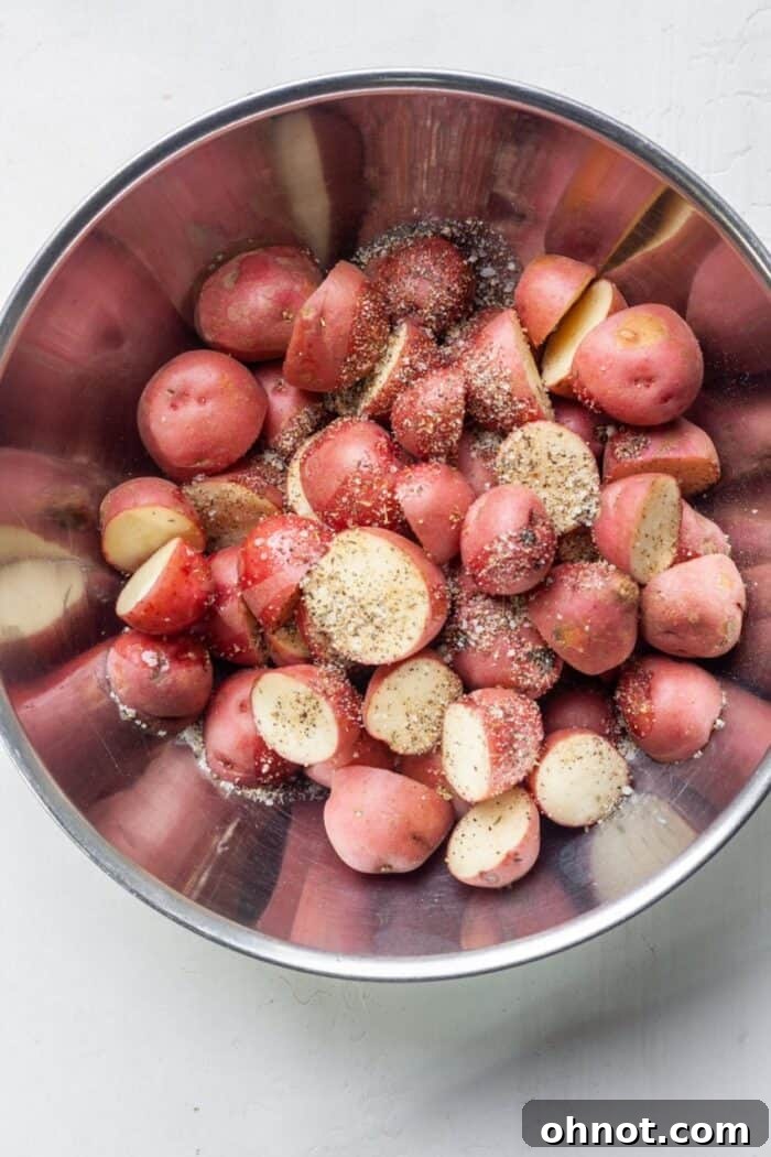 Cubed red potatoes in a bowl with oil and seasonings, ready to be tossed for even coating