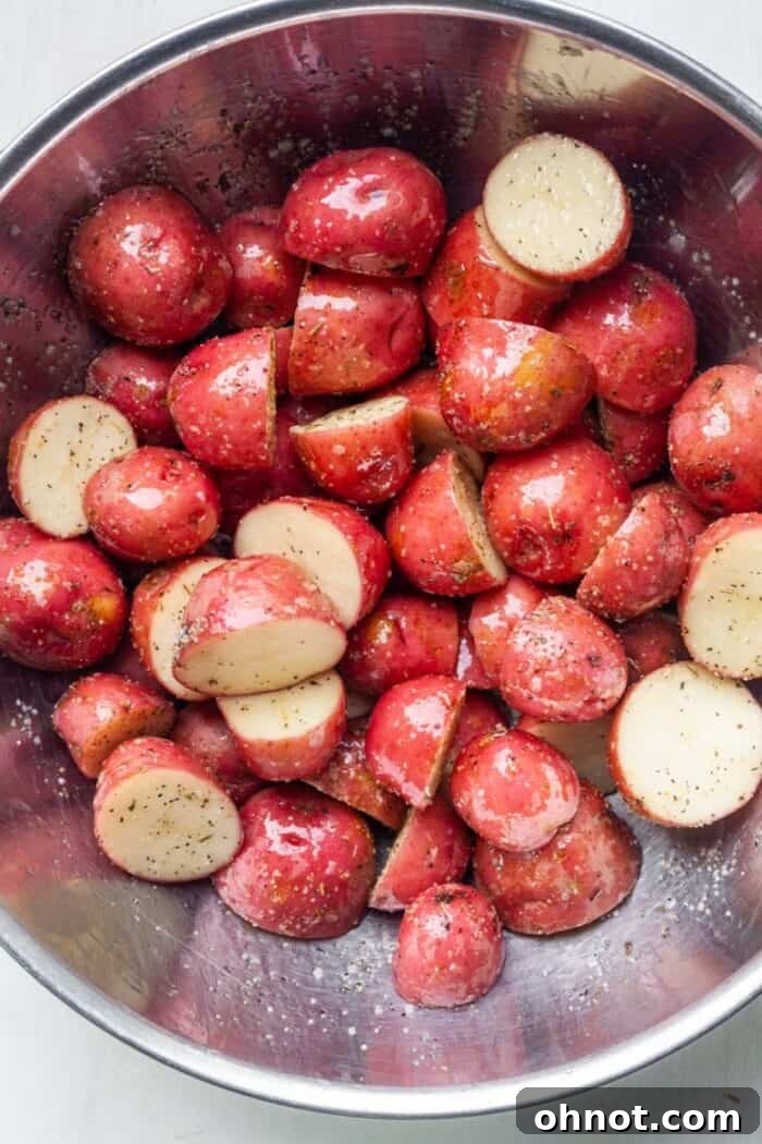 Close-up of diced potatoes thoroughly coated in olive oil and seasonings in a mixing bowl