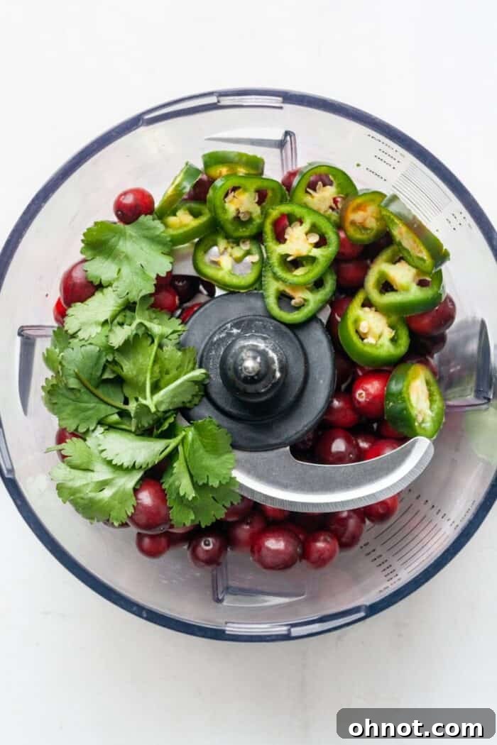 Fresh cranberries and sliced jalapeños being added to a food processor