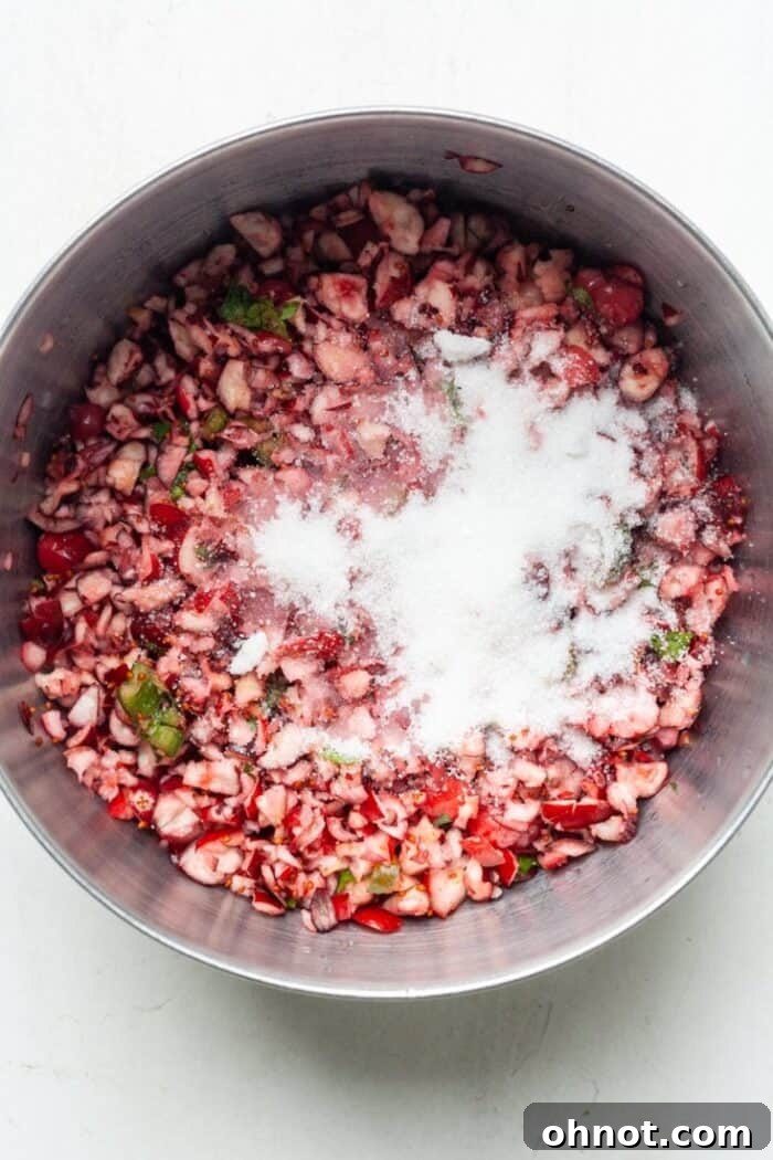 Granulated sugar being added to the bowl with the cranberry, jalapeño, and cilantro mixture
