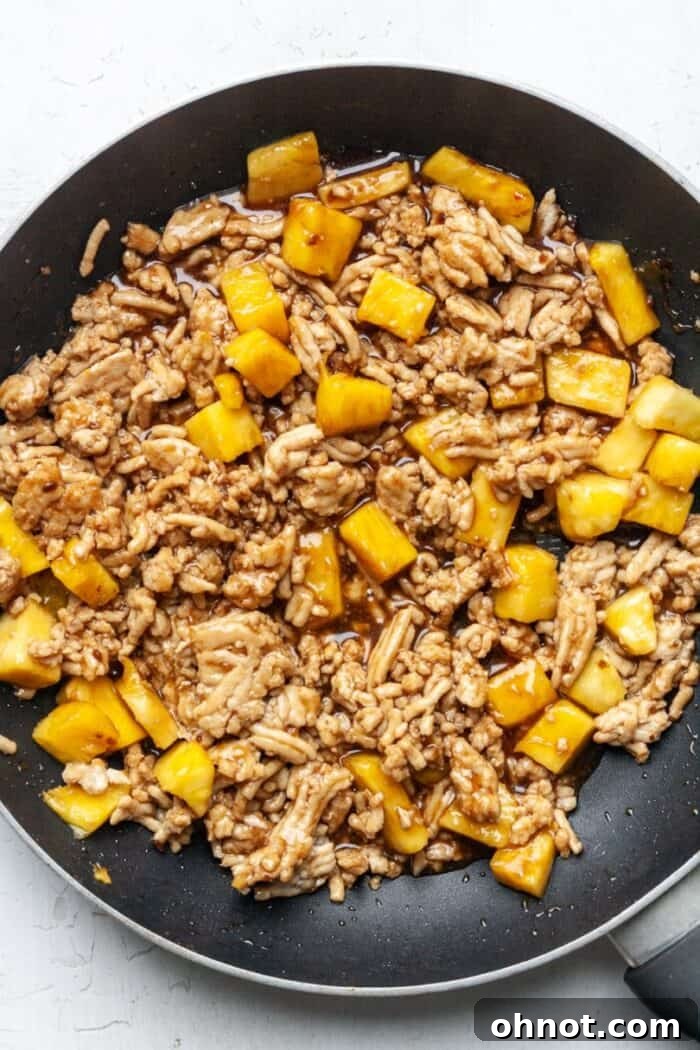 Ground chicken and diced pineapple mixed with teriyaki sauce in a skillet.