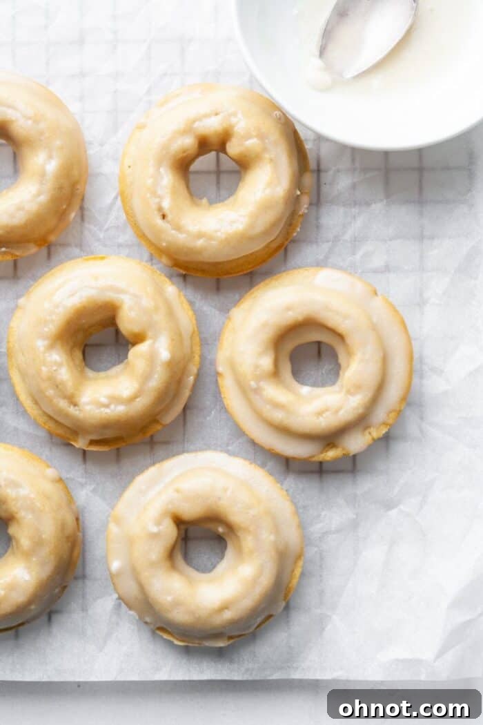 Several vanilla glazed gluten-free donuts resting on a wire rack, allowing the glaze to set.