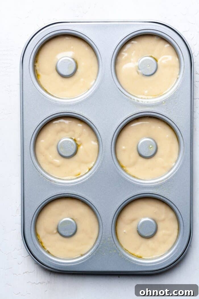 Raw gluten-free donut batter carefully spooned into a greased donut pan, filling each cavity halfway.