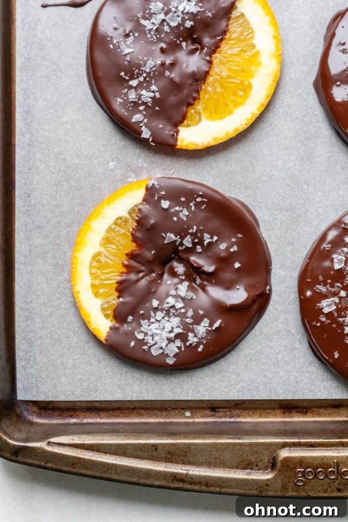 Dark chocolate coating freshly applied to orange slices on parchment paper.