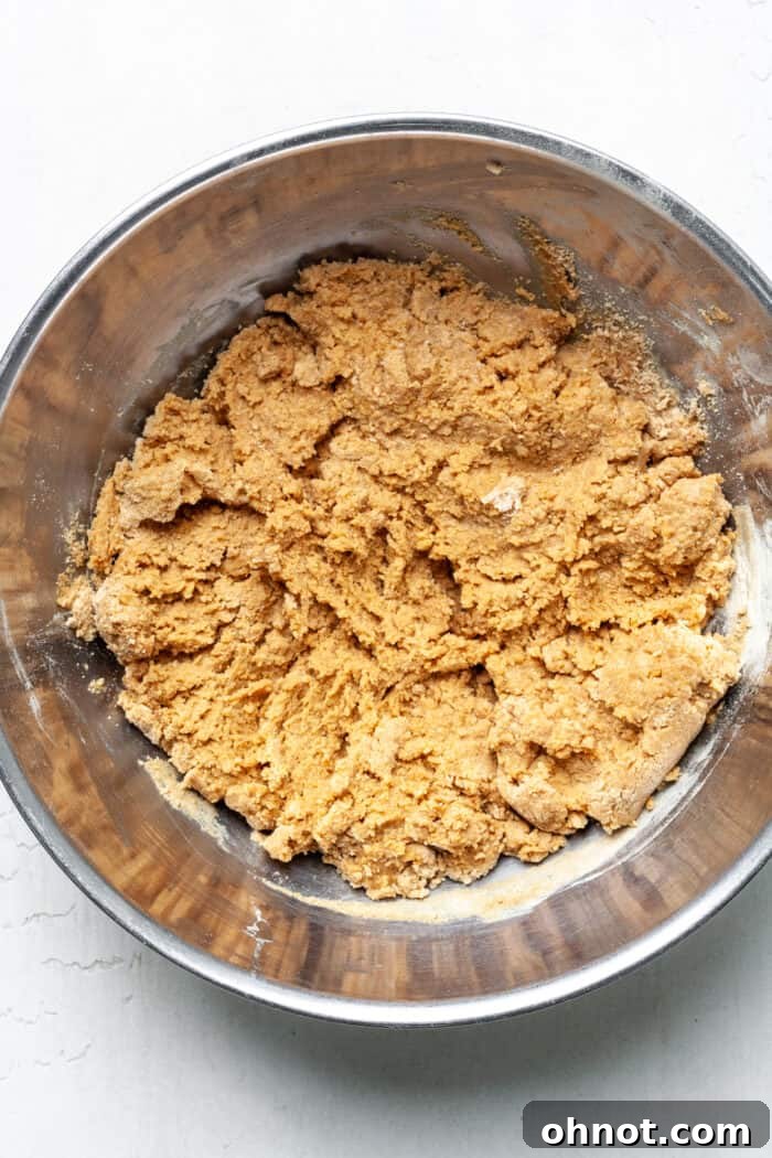 Thick, golden-brown peanut butter cookie dough forming in a mixing bowl, prior to the addition of chocolate chips.