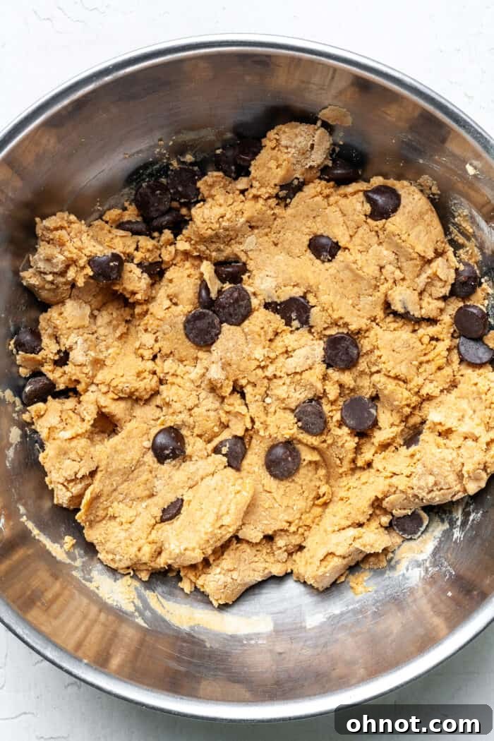 Thick cookie dough in a mixing bowl with dark chocolate chips folded in, ready for scooping.