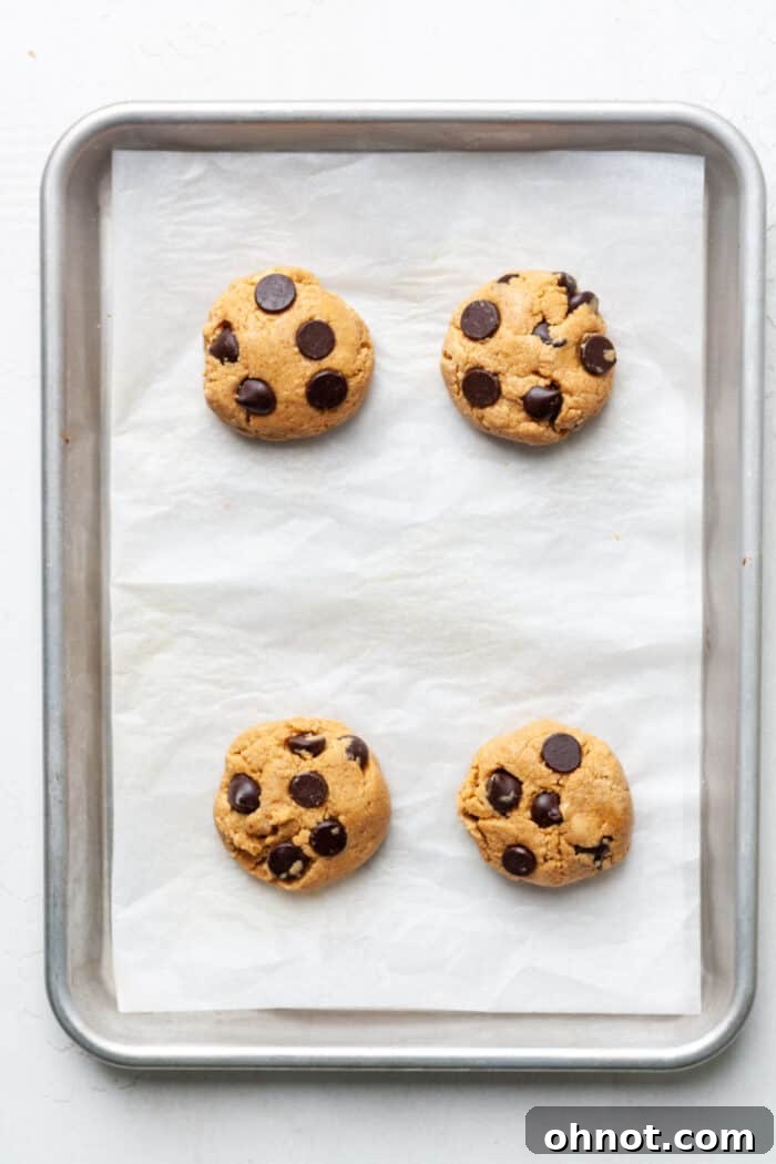 Unbaked protein cookies, shaped into flat discs, arranged on a parchment-lined baking pan, ready for the oven.