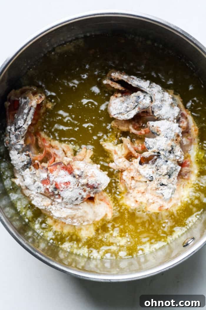 Lobster tails being carefully placed into a pot of hot oil for deep frying.