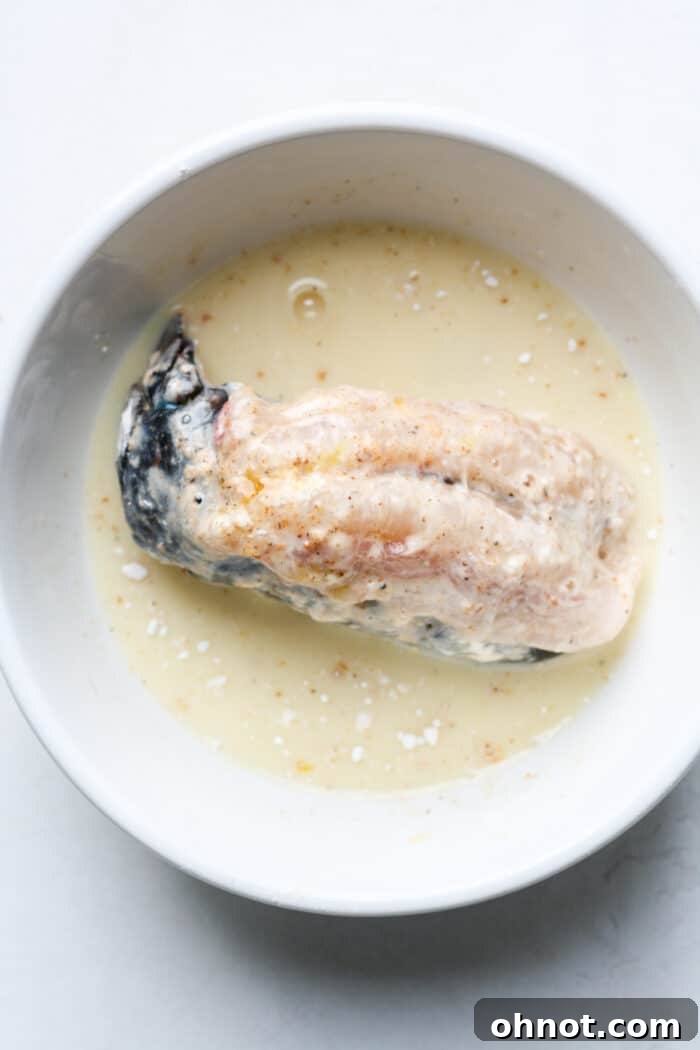 A lobster tail being dipped into the egg wash mixture.