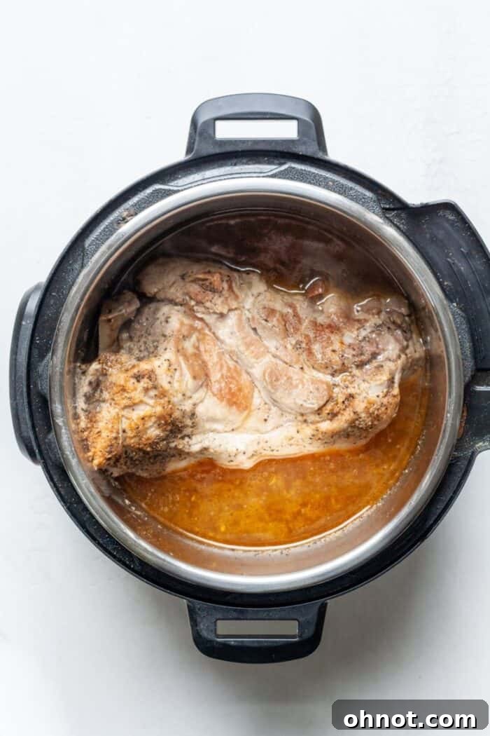 Tender cooked pork being shredded in the Instant Pot with two forks