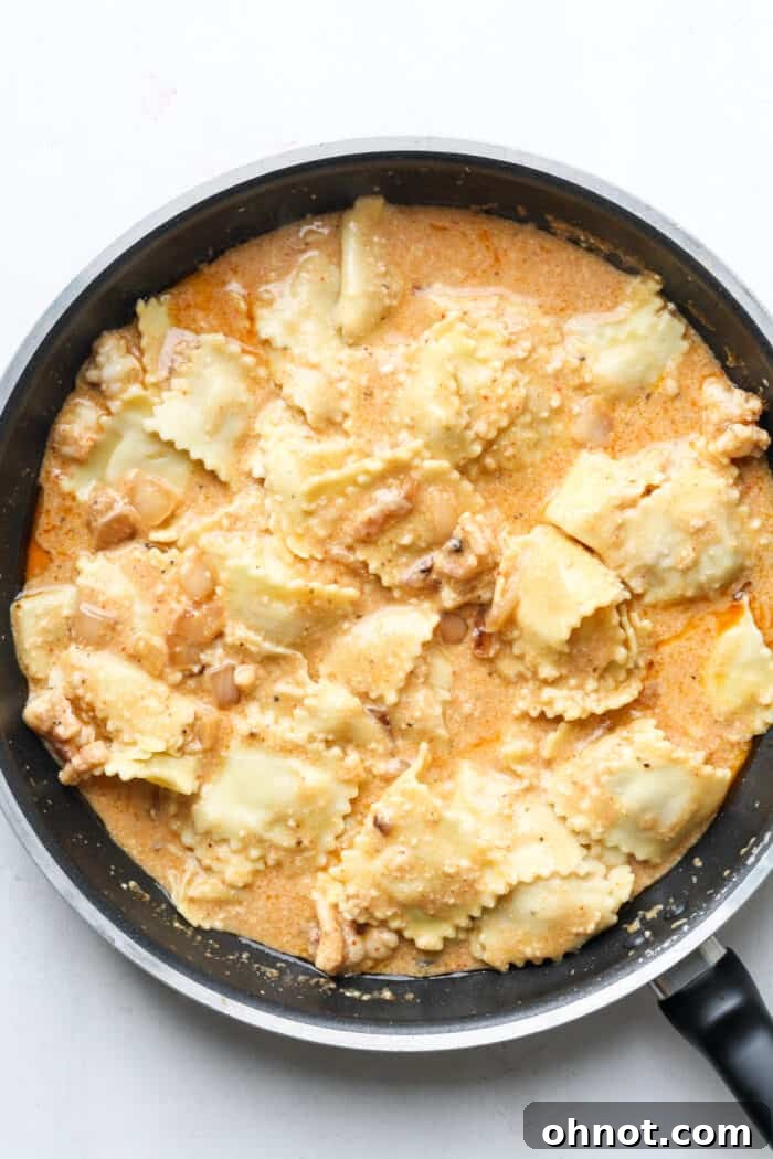 Cooked ravioli being tossed in the creamy lobster sauce in a skillet.