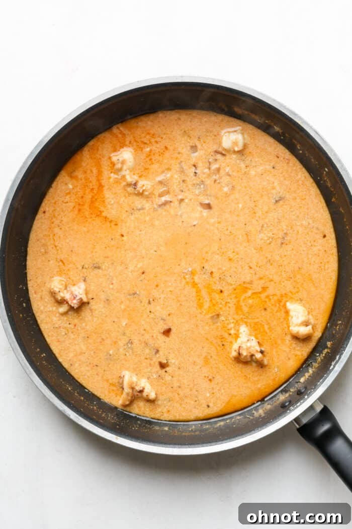 The cream sauce simmering, taking on an orange hue from the Old Bay seasoning.
