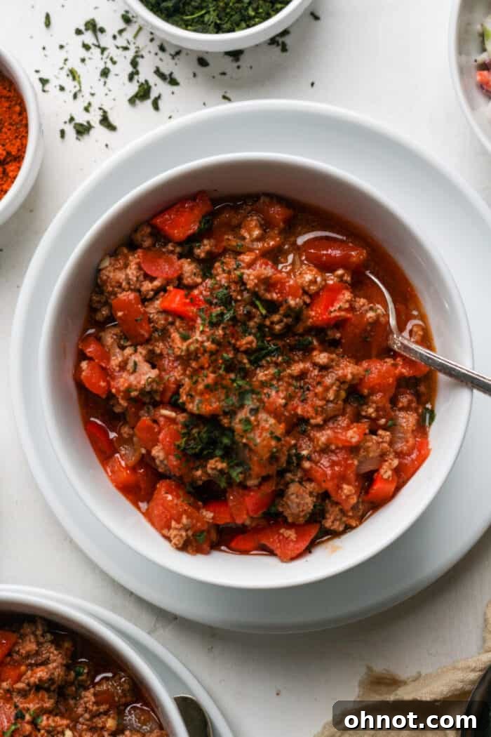 A warm bowl of Dutch oven chili, garnished with fresh cilantro and a dollop of sour cream, resting on a rustic wooden table.
