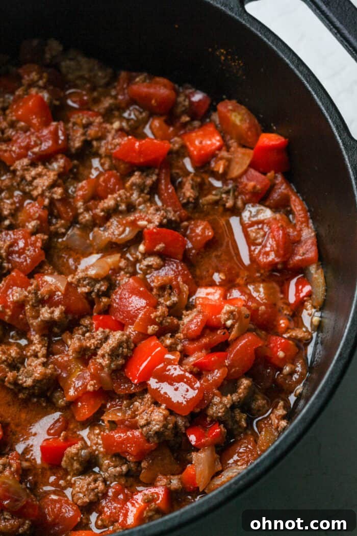 A large Dutch oven filled with simmering chili, with a ladle resting inside, ready for serving.
