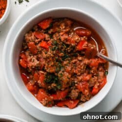 Dutch oven chili in white bowl, garnished with fresh herbs and a spoon.