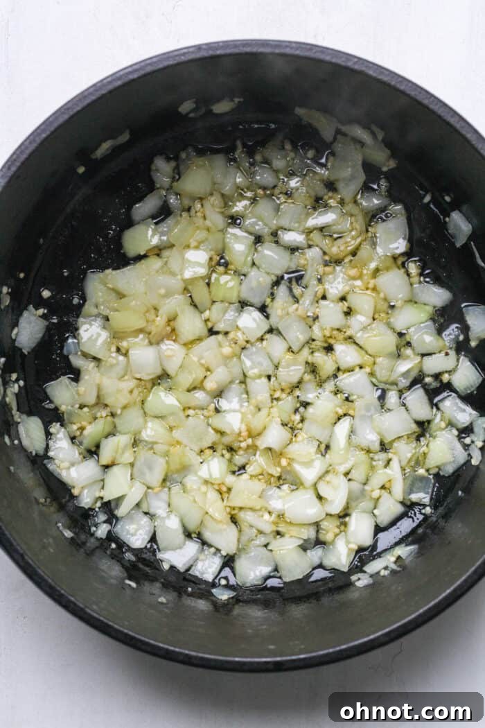 Close-up of softened, translucent onions and garlic in a Dutch oven, ready for the next step.
