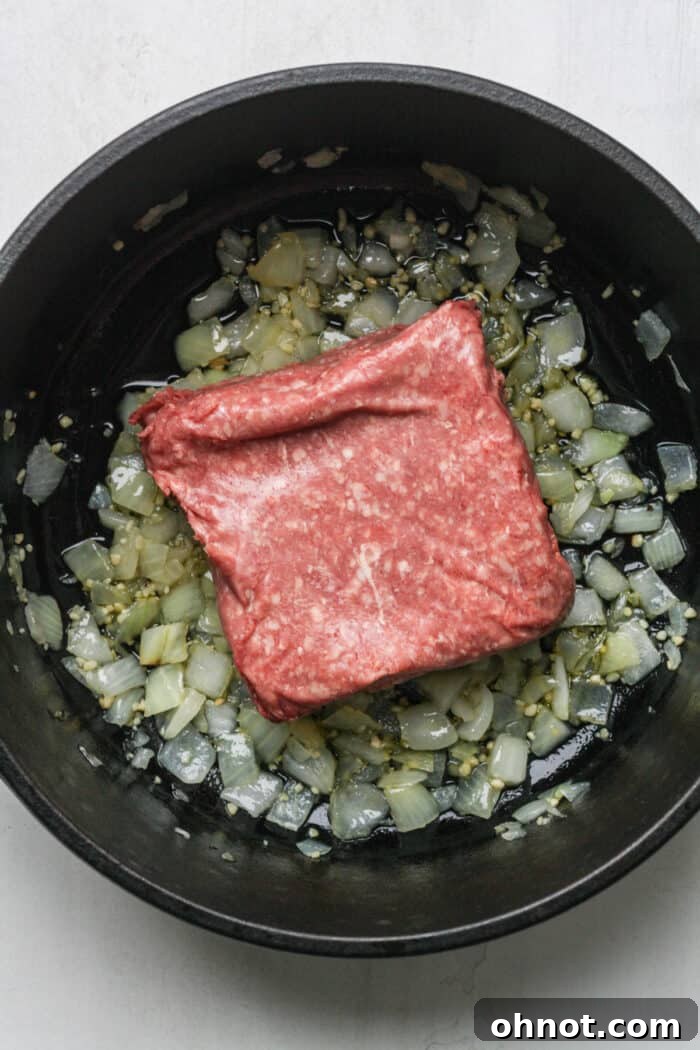 Ground beef cooking in a Dutch oven, starting to brown and separate.