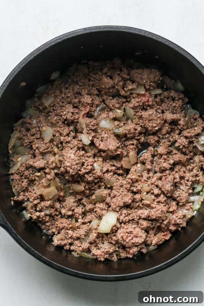A mix of browned ground beef and softened onions in a Dutch oven, well combined.