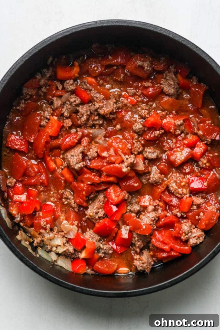All chili ingredients, including ground beef, tomatoes, and spices, mixed together in a Dutch oven before simmering.