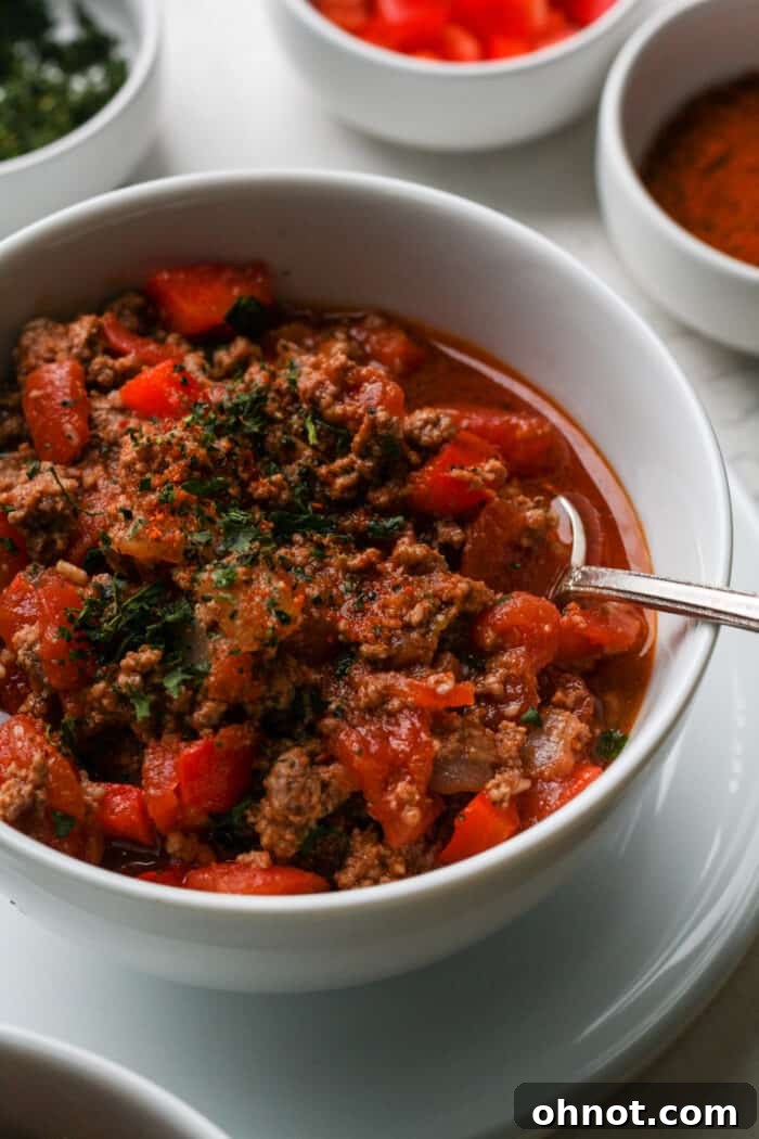Two white bowls filled with hearty Dutch oven chili, topped with fresh garnishes, ready to be served.