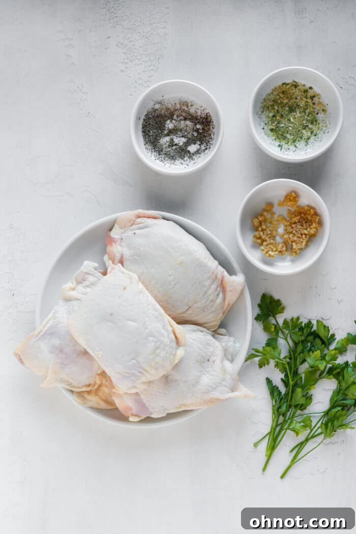 Fresh ingredients laid out for sous vide chicken thighs: chicken thighs, onion powder, sea salt, pepper, minced garlic, and fresh herbs