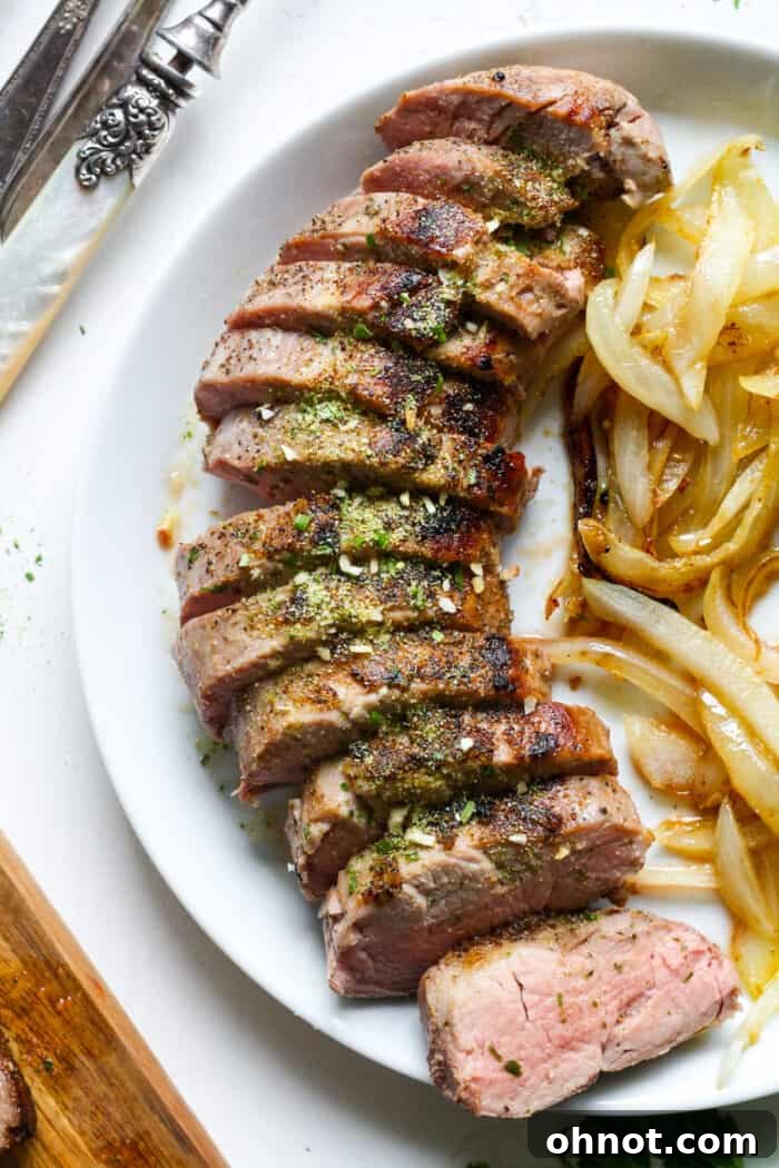 Perfectly cooked Sous Vide Pork Tenderloin, sliced and served on a white plate with fresh herbs.