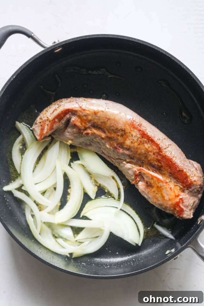 Pork tenderloin with sliced onions and minced garlic cooking in a skillet.