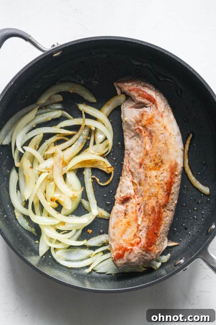 Closer view of pork tenderloin with softened onions and garlic in the pan.