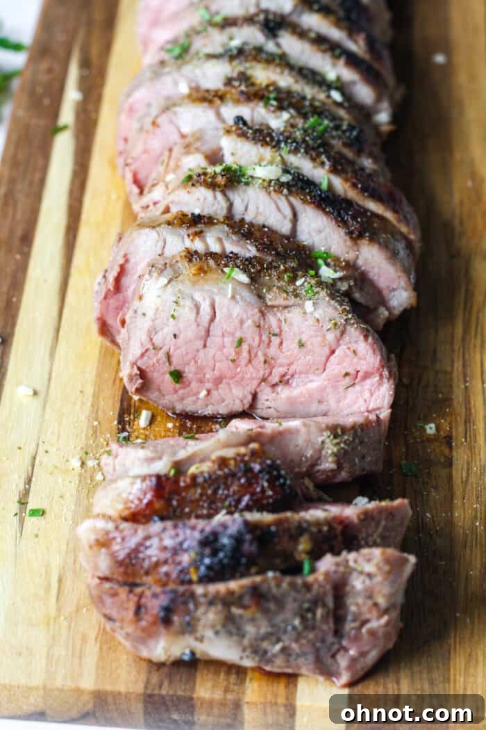 Sliced sous vide pork tenderloin resting on a wooden cutting board, garnished with fresh herbs.