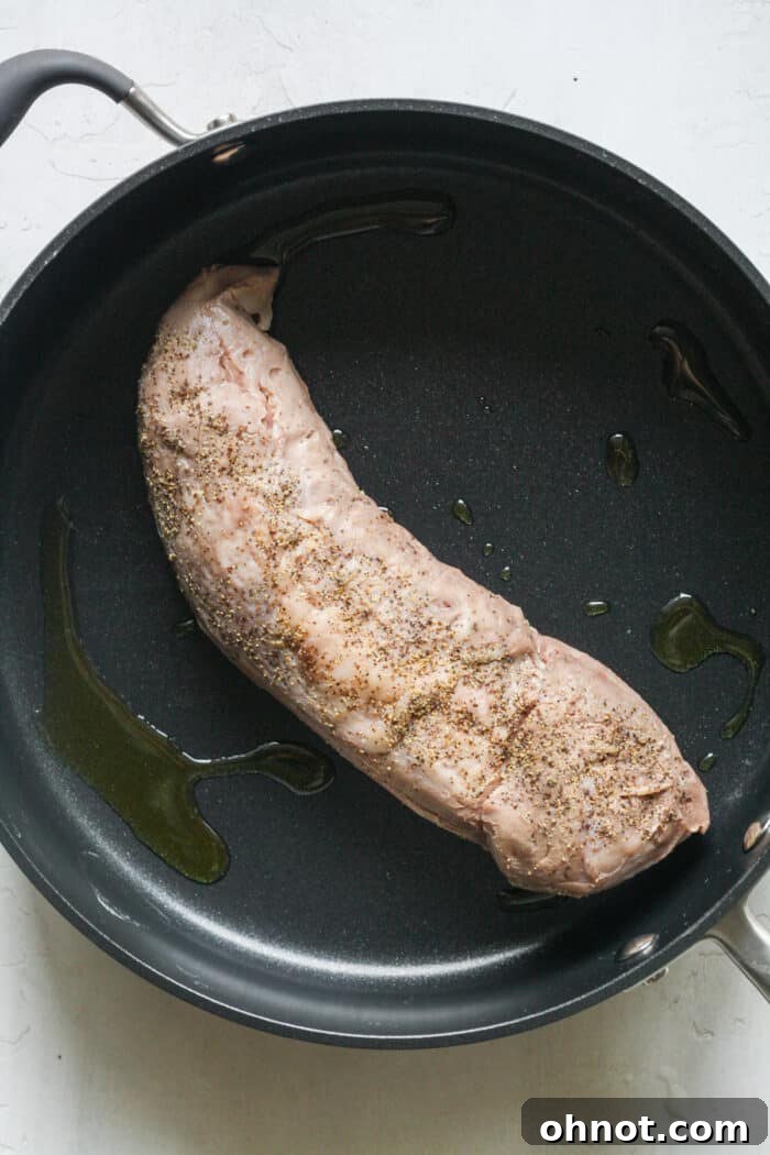 Pork tenderloin searing in a hot skillet with olive oil.