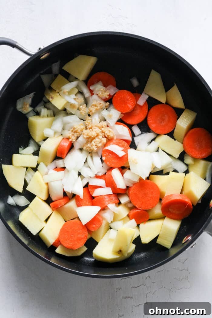 Freshly chopped potatoes, carrots, onion, and garlic in a skillet before cooking.