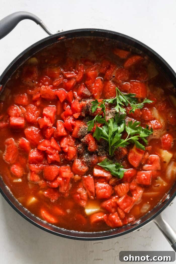 Diced tomatoes and broth added to the sautéed vegetables in the skillet, starting to simmer.