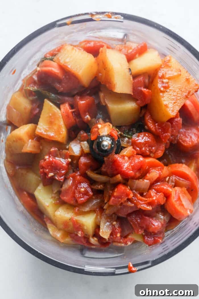 Cooked vegetables and liquid in a food processor, ready to be blended into soup.