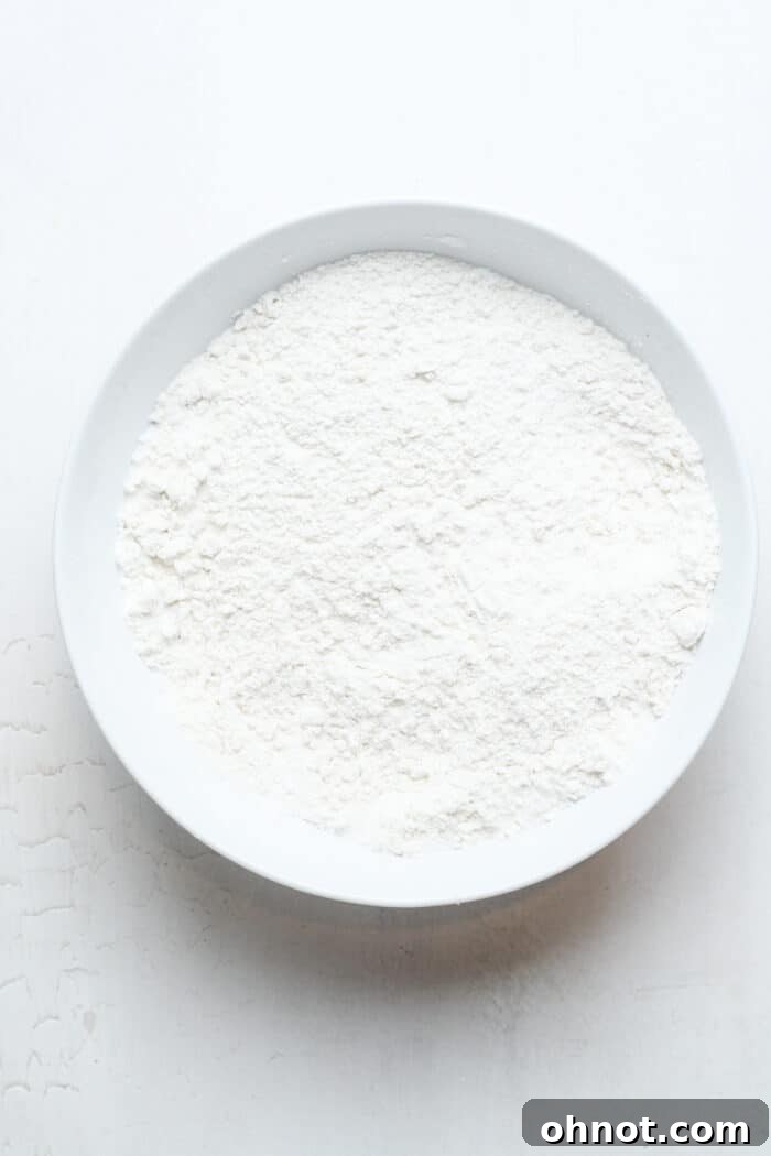 Gluten-free flour, baking powder, and sugar in a white bowl, ready to be whisked.
