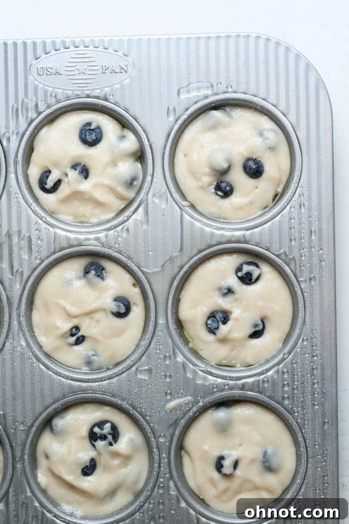Raw muffin batter neatly scooped into a greased muffin pan, ready for baking.