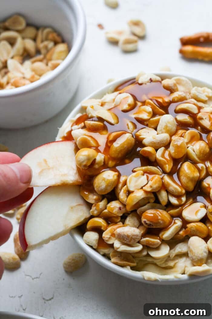 A generous serving of creamy caramel apple dip in a white bowl, elegantly drizzled with extra caramel and topped with crunchy peanuts, ready to be enjoyed.