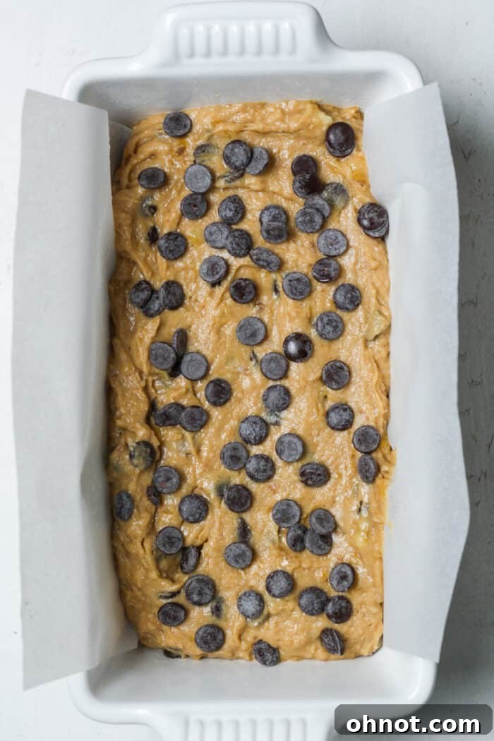 Unbaked vegan banana bread batter, studded with chocolate chips, neatly placed in a parchment-lined loaf pan.