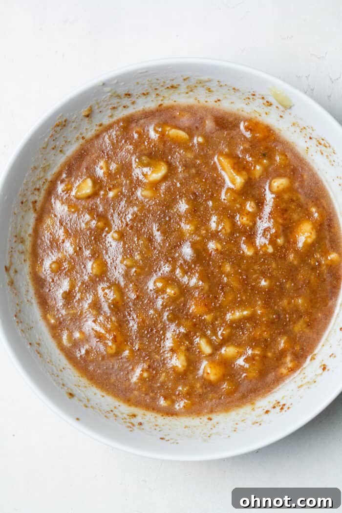 All wet ingredients mixed together in a large white bowl, forming a smooth banana mixture.