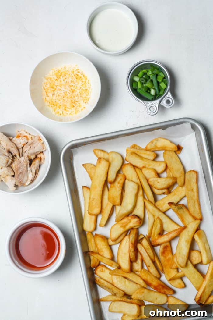 A selection of fresh ingredients including French fries, cheese, and buffalo sauce laid out on a clean surface.