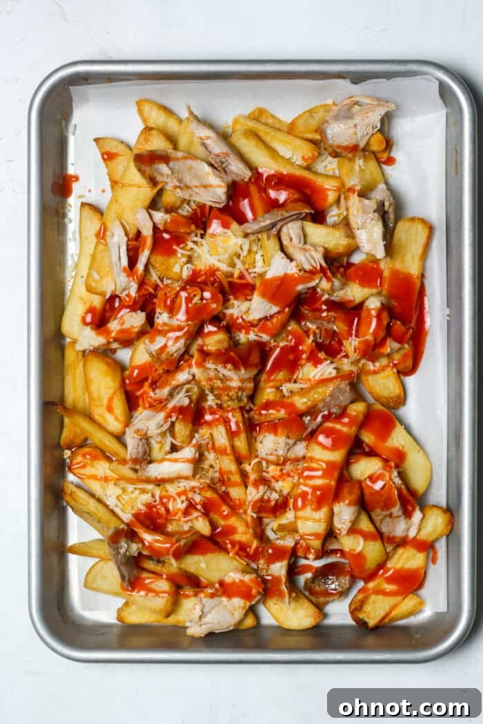 Hot buffalo sauce being drizzled over the chicken and fries.