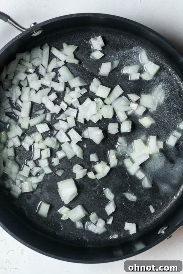Finely diced white onions glistening in a hot skillet with melted butter.