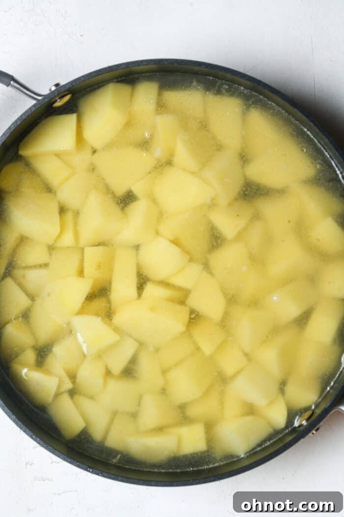 Cubed Russet potatoes submerged in water within a large skillet, ready for boiling.