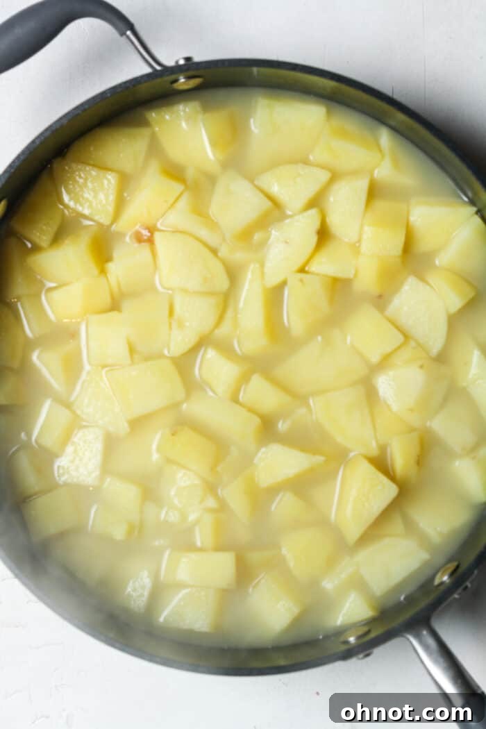Boiling potatoes bubbling vigorously in a skillet on the stovetop, close to being fork-tender.