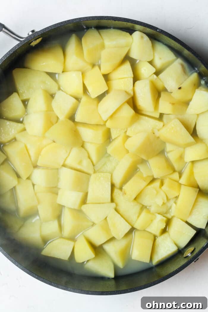 Tender cooked potatoes in a skillet with a small amount of reserved cooking water.